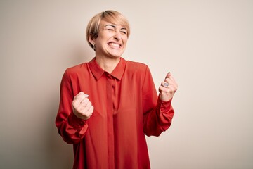 Wall Mural - Young beautiful business blonde woman with short hair standing over isolated background excited for success with arms raised and eyes closed celebrating victory smiling. Winner concept.