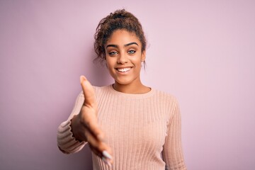 Sticker - Young beautiful african american girl wearing casual sweater standing over pink background smiling friendly offering handshake as greeting and welcoming. Successful business.