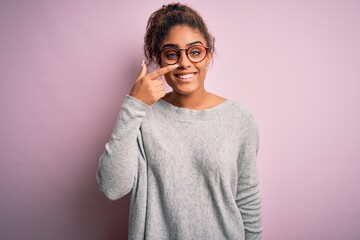 Canvas Print - Young beautiful african american girl wearing sweater and glasses over pink background Pointing with hand finger to face and nose, smiling cheerful. Beauty concept