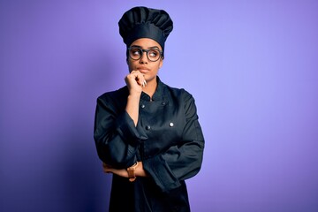 Poster - Young african american chef girl wearing cooker uniform and hat over purple background with hand on chin thinking about question, pensive expression. Smiling with thoughtful face. Doubt concept.