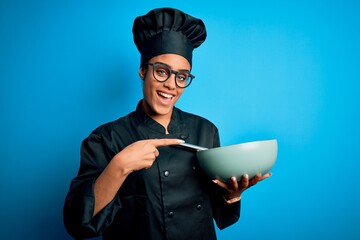 Poster - Young african american chef girl wearing cooker uniform and hat using whisk and bowl very happy pointing with hand and finger