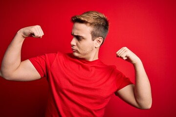 Wall Mural - Young handsome redhead man wearing casual t-shirt over isolated red background showing arms muscles smiling proud. Fitness concept.