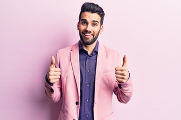 Young handsome man with beard wearing elegant jacket success sign doing positive gesture with hand, thumbs up smiling and happy. cheerful expression and winner gesture.