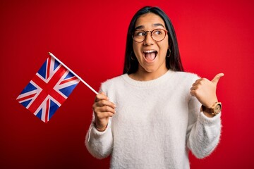 Poster - Young asian woman holding united kingdom flag for brexit referendum over red background pointing and showing with thumb up to the side with happy face smiling