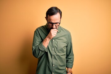 Canvas Print - Middle age hoary man wearing casual green shirt and glasses over isolated yellow background feeling unwell and coughing as symptom for cold or bronchitis. Health care concept.