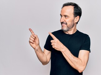 Poster - Middle age man wearing casual black t-shirt standing over isolated white background smiling and looking at the camera pointing with two hands and fingers to the side.