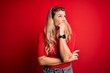 © Krakenimages.com - Young beautiful blonde woman wearing casual t-shirt standing over isolated red background Thinking worried about a question, concerned and nervous with hand on chin