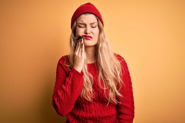 Canvas Print - Young beautiful blonde woman wearing casual sweater and wool cap over white background touching mouth with hand with painful expression because of toothache or dental illness on teeth. Dentist