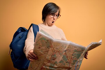 Wall Mural - Young down syndrome tourist woman wearing bag and looking at destination city map scared in shock with a surprise face, afraid and excited with fear expression