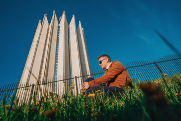 A young man boy sits in a field of dandelions on a Sunny happy day against the backdrop of a futuristic sk