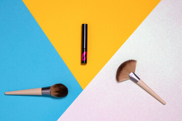 Two professional makeup brushes and a lipstick flat lay on a bright pink, yellow and blue background with copy space. Template for cosmetics product display montage or advertising text. Beauty and sk