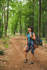 Wall Mural - young adult woman walking with backpack by forest trail