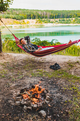 Wall Mural - man laying on hammock at lake beach near camp fire