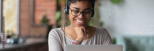 Cuadros en Lienzo African girl wear headphones looks at pc screen watch movie, online webinar, enj