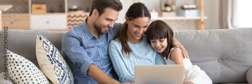 Cuadros en Lienzo Couple and little daughter sit on sofa using pc watching cartoons on-line, surfing internet, buying via e-commerce web sites, spend weekend at home