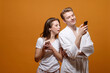 © denisval - man and woman with phones in hands on yellow background, woman indignantly looks at phone of man