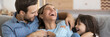 © fizkes - Laughing husband and daughter tickling mother family play together having fun resting on sofa at home close up photo. Weekend activities, affection concept. Horizontal banner for website header design