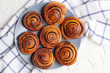Wall Mural - baked cinnamon buns on grey plate on light background with checkered napkin