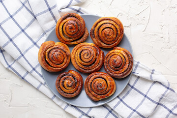 Wall Mural - baked cinnamon buns on grey plate on light background with checkered napkin