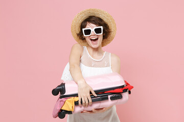 Wall Mural - Excited tourist woman in summer white dress hat sunglasses isolated on pink background in studio. Female traveling abroad to travel weekend getaway. Air flight journey concept. Hold opened suitcase.