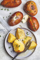 Canvas Print - Baked potatoes with butter and thyme on gray plate, top view.