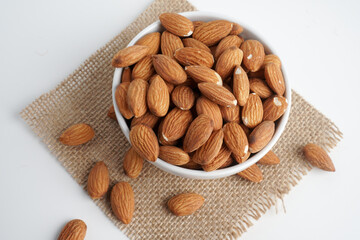 Wall Mural - almonds in white bowl and glass of milk and brown fabric on white background. top view and flat lay, 