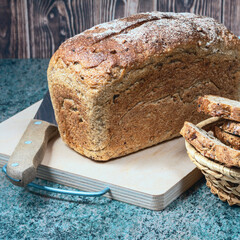 Poster - sliced ​​bread in a wicker basket and a loaf of wheat bread with baked shiny crust on the kitchen table