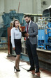 © VItaliy - Portrait of a solid businessman with his secretary holding laptop and tablet, talking about factory financial report. Industrial workers.