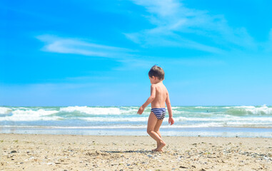 A little boy is walking on the seashore. A child on a tropical beach. Sand and water are fun, sun protection for young children.