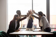Multi-ethnic diverse group of businesspeople workmates celebrating common success gathered in board room stack palms together giving high five share achievements happy moment, team building concept