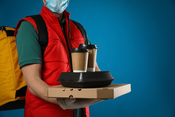 Canvas Print - Courier in protective mask and gloves holding order on blue background, closeup. Food delivery service during coronavirus quarantine