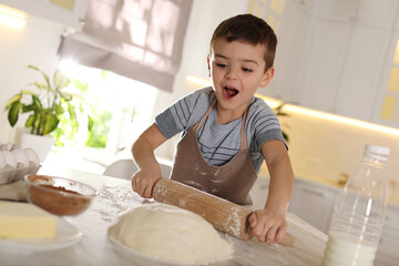 Poster - Emotional little boy rolling dough at table in kitchen. Cooking pastry