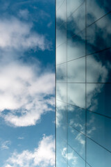 A blue sky and a modern blue glass facade in which clouds are reflected.