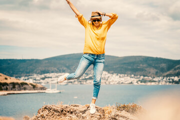 Happy young woman in a yellow shirt and hat rejoices on the seashore with a view, summer vacation and travel. Image with retro toning.