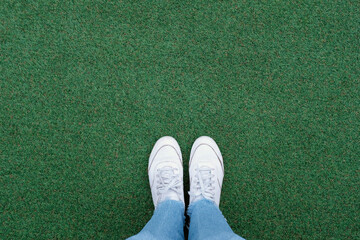 Selfie of feet in white sneakers shoes on green grass background with copy space, spring and summer with fashion lifestyle concept