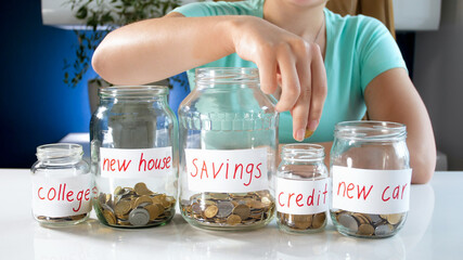 Young woman filling glass jars with money savings. Concept of financial investment, economy growth and bank savings