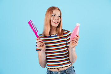 Poster - Image of joyful charming girl holding shampoo and comb while smiling