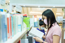 An Asian Woman Shopping In The Book Shop After Opening Lockdown With Pink Mask And Social Distancing.