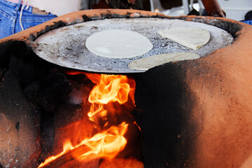 
handmade tortillas made by hand, in a red stone oven with a fire flame heating the comal, typical Mexican food.