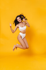 Wall Mural - Image of young happy woman in swimsuit jumping and showing thumbs up