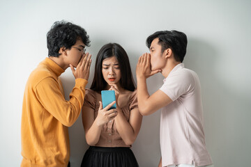 Wall Mural - two young men whispering to a young girl using a smart phone while standing against an isolated background