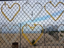 Yellow And White Plastic Bag Hearts On Metal Chain Link Fence At Beach