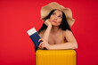 Travel concept. Studio portrait of pretty young woman holding passport and luggage. Isolated on red