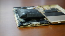 Swollen Smartphone Battery. Damaged Smartphone With A Faulty Battery. Damaged Phone On A Wooden Background.