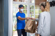Repartidor con mascarilla entregando comida para llevar en bolsas de cartón en la puerta de una casa
