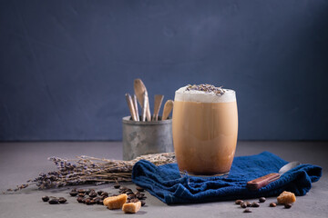 Latte with milk foam and lavender in a glass with coffee beans. Dark background