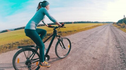 Wall Mural - Woman ride a bike. Young woman rides a bike on the rural road in the field during sunny day