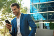 © mavoimages - Smiling businessman sitting outside reading a text on his cellphone