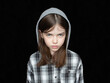 portrait of a little offended tearful girl in a hoodie on a black background