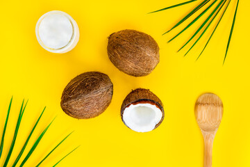 Top view organic bio coconut butter with two whole fresh coconuts, one half and palm leaves on yellow background. Natural oil for cooking and skincare beauty. Flatlay.